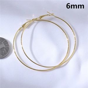 Macro detail of large 6mm gold hoop earrings on textured white background