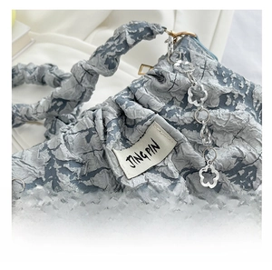 Detail of light blue ruched fabric texture with silver floral chain and Jing Pin logo