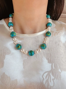 Model wearing pearl and turquoise glass bead necklace with vintage floral patterns