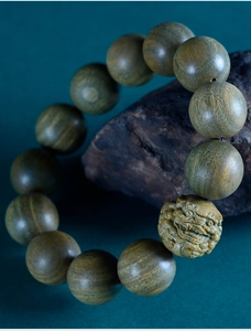 Detail of sandalwood beads featuring an intricately carved Pixiu charm on a dark rock