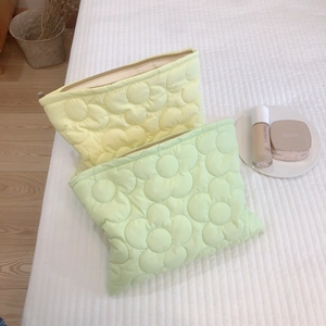Quilted floral puffer cosmetic bags in soft yellow and mint green on a white bed