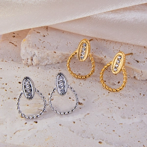 Twisted geometric gold and silver stud earrings with zircon crystals on stone background