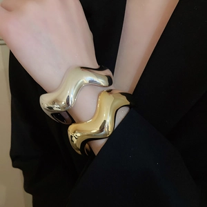 Dettaglio di bracciali aperti a onde sovrapposti in oro e argento con finitura lucida