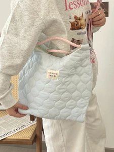 Light blue quilted heart tote bag with pink braided handles and colorful logo patch