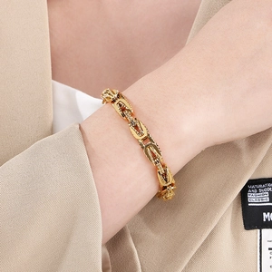 Close-up of gold textured emperor chain bracelet on model wrist with beige suit jacket