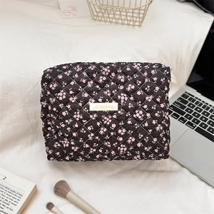 Detailed close-up of a black quilted floral makeup bag on a white bedding background