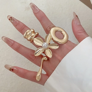 Close-up of golden alloy rings with flower design and liquid drop pendant on hand
