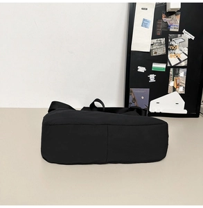 Flat view of a black nylon crossbody tote bag showing its durable bottom construction