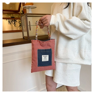 Détail du sac cabas en toile à carreaux rouges avec poche en denim et anses tissées