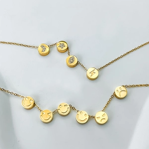 Collana dorata multi-ciondolo con stelle, lune in zircone ed emoji su sfondo di pietra