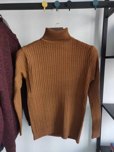 Dettaglio di un maglione marrone a dolcevita con trama classica a trecce e maglia