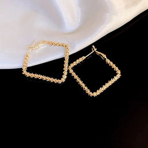 Detailed close-up of textured golden square hoop earrings on a black reflective surface