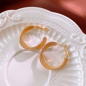 Detailed close-up of golden beaded hoop earrings on vintage relief ceramic plate