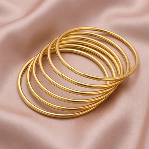 Macro view of several 3mm gold stainless steel bangles stacked on soft pink silk