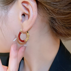 Gros plan de créoles en forme de C en émail rouge et métal doré portées par un mannequin