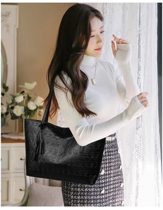 Close-up of black tote bag featuring embossed skull pattern and leather tassel detail
