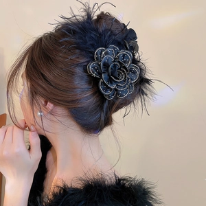 Detail of a black fabric camellia hair claw with rhinestones and feathers on a model