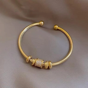 Close-up of gold-plated open bangle with crystal pavé cylinder and polished beads