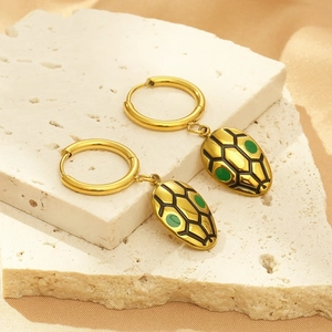 Gold hoop earrings with green-eyed snake pendants on a textured stone display