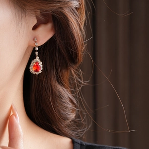 Detail of a red teardrop pendant earring with small diamonds on model ear