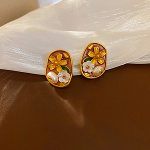 Detailed close-up of gold flower earrings with enamel petals and pearls on dark leather