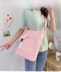 Detailed view of pink canvas crossbody bag with white NICE text and side pocket detail