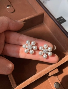 Gros plan de boucles d'oreilles fleur en perles avec centre en zircon dans une main