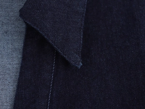 Gros plan sur le tissu denim bleu foncé d'une robe montrant texture et surpiqûres