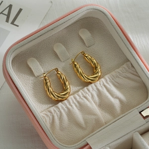 Boucles d'oreilles créoles torsadées en U dorées dans un écrin sur tissu blanc