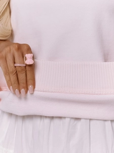 Gros plan d'une bague ours en résine rose et d'un anneau minimaliste sur une main