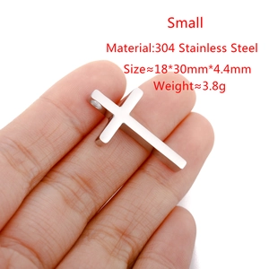 Polished stainless steel cross pendant shown in hand for size scale and metal texture