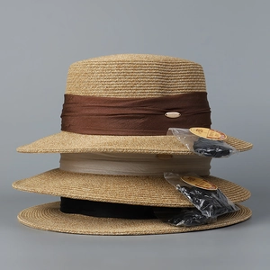 Détail de chapeaux de paille plats empilés avec rubans en satin et étiquettes UPF 50+