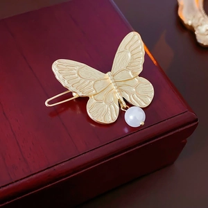 Detailed view of a golden butterfly hair clip with a white pearl on a wooden jewelry box