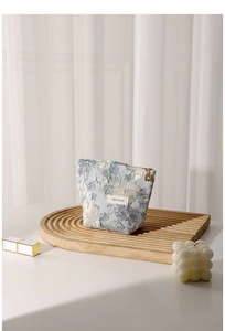 Detail of floral jacquard makeup bag with brand label on a wooden tray with candle