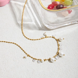 Elegant gold pearl necklace with crystal charms on textured surface with glass jar