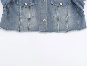 Detail of washed blue denim jacket featuring chest pockets and distressed raw hem edges