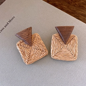 Makro-Detail von geometrischen Ohrringen mit braunem Holzdreieck und beigem Strohgeflecht