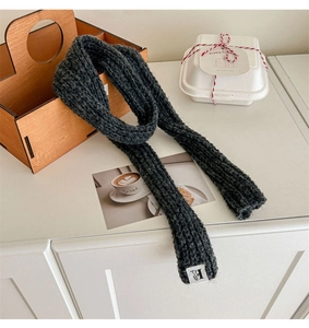 Macro detail of dark grey knit wool scarf texture with a white minimalist 'H' logo tag