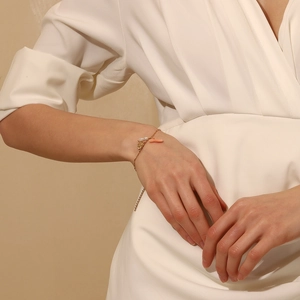 Detailed close-up of 18K gold plated bracelet with pearl and coral charms on a model wrist