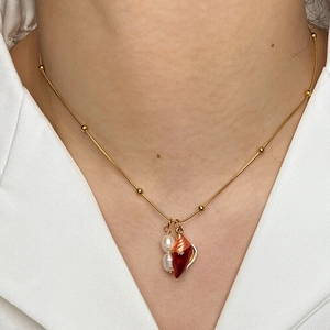 Gold snake chain necklace with conch pendant and pearls worn by a model in a white shirt