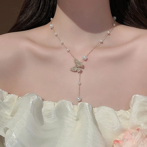 Detail einer goldenen Schmetterlingskette mit Zirkonsteinen und Perlenquasten am Hals