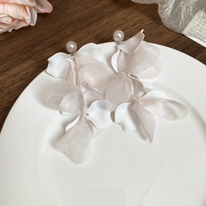 Detailed shot of white fabric flower earrings with pearls on a ceramic plate