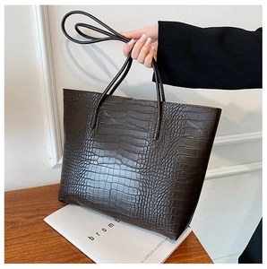 Detailed close-up of dark brown crocodile embossed leather tote bag on wooden surface