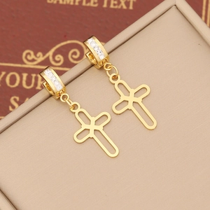 Macro shot of gold-plated cross earrings with white zircon accents on a beige display