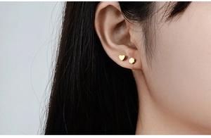 Close-up of minimalist gold heart and geometric stud earrings on a model's ear