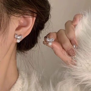 Detailed view of silver butterfly zircon earrings with white pearls on a model and hand
