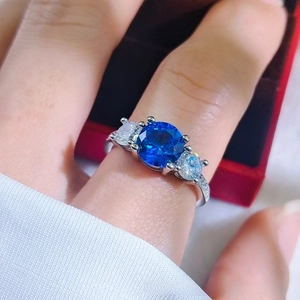 Macro view of three-stone ring with dark blue center gem and pave diamond band