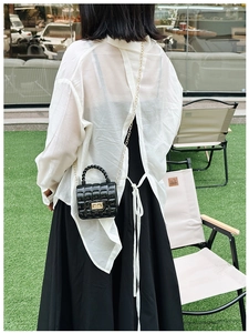 Close-up of black quilted jelly handbag with golden chain strap on a green lawn