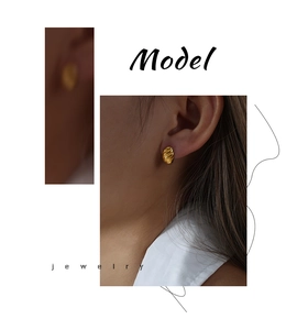 Close-up of a model wearing a golden C-shaped twisted hoop earring with a metallic finish