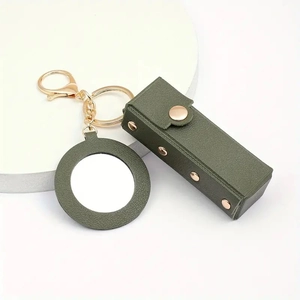 Close-up of green leather lipstick holder and round mirror with gold metal keychain